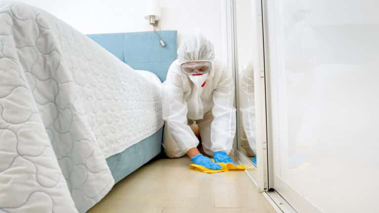 Housekeeper or maid in hotel wearing protective medical suit and mask washing and cleaning floor in room. Disinfection in hotels